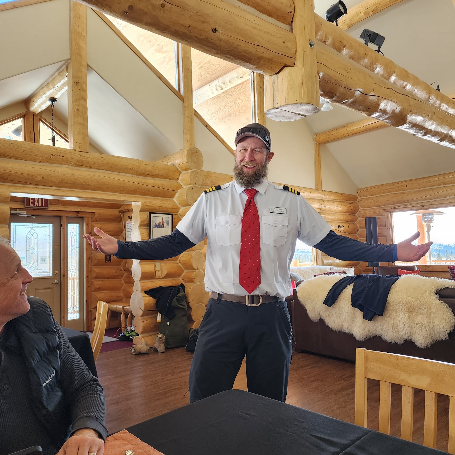A host in a pilot's uniform welcomes the group in the lodge's log-cabin dining room