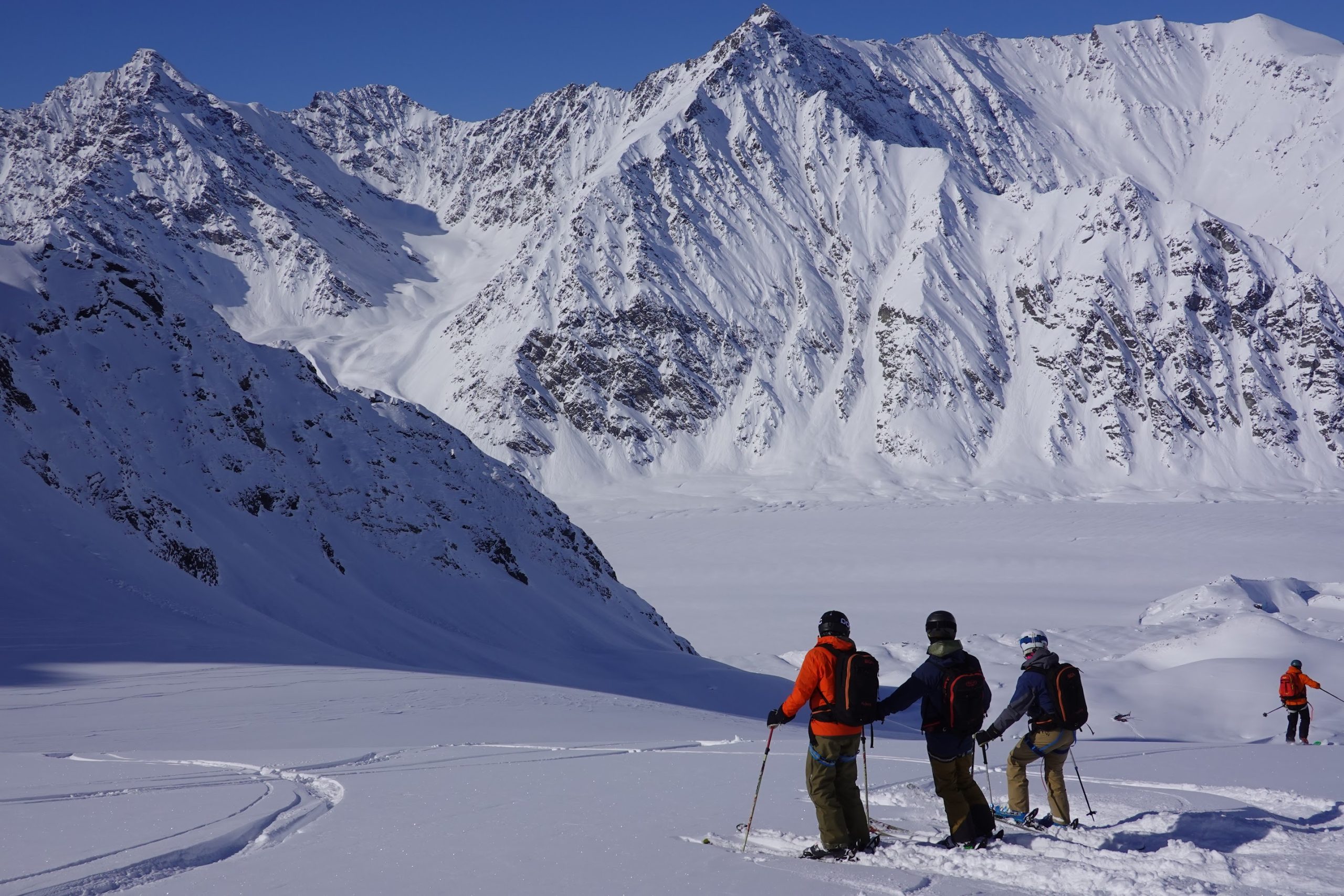 Skiers with backpacks look out over a snowy Alaskan glacier valley
