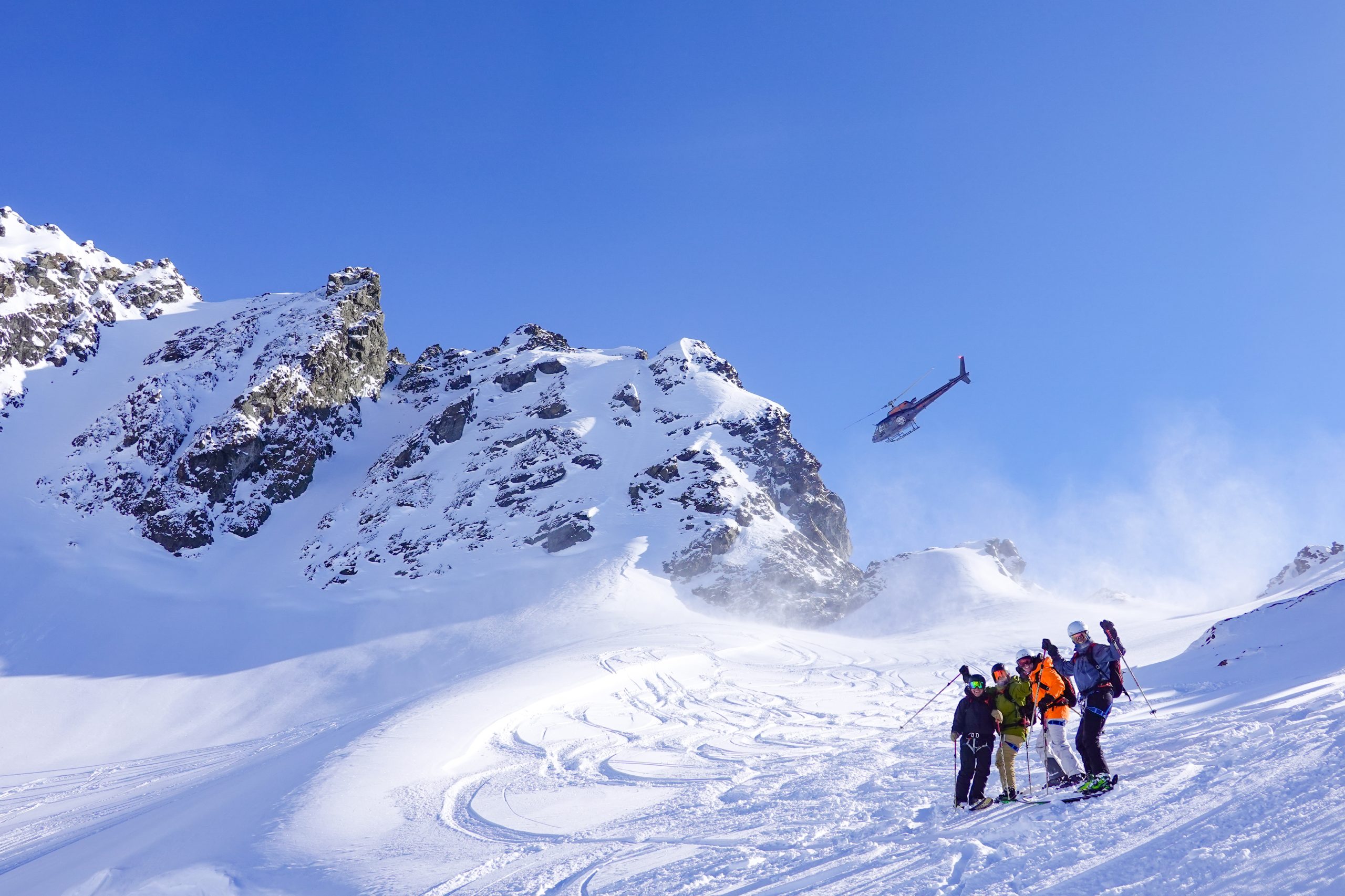 A helicopter lifts off behind a group of skiers on a snowy Alaskan ridge