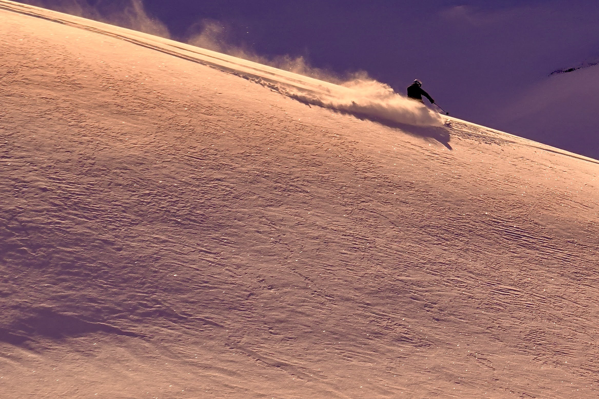A skier sprays powder on a sunlit slope