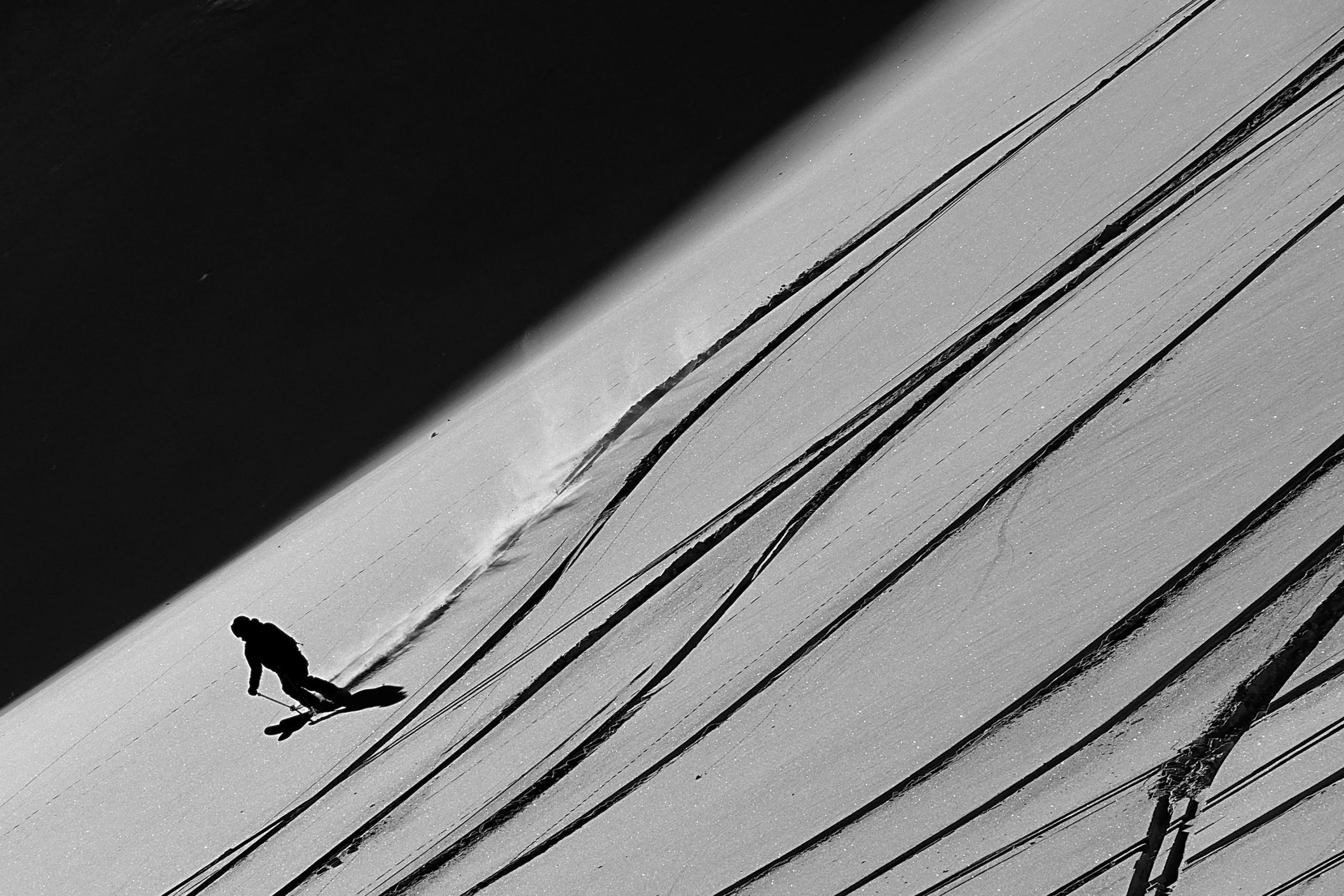 Black-and-white photo of a skier carving down a steep slope lined with ski tracks