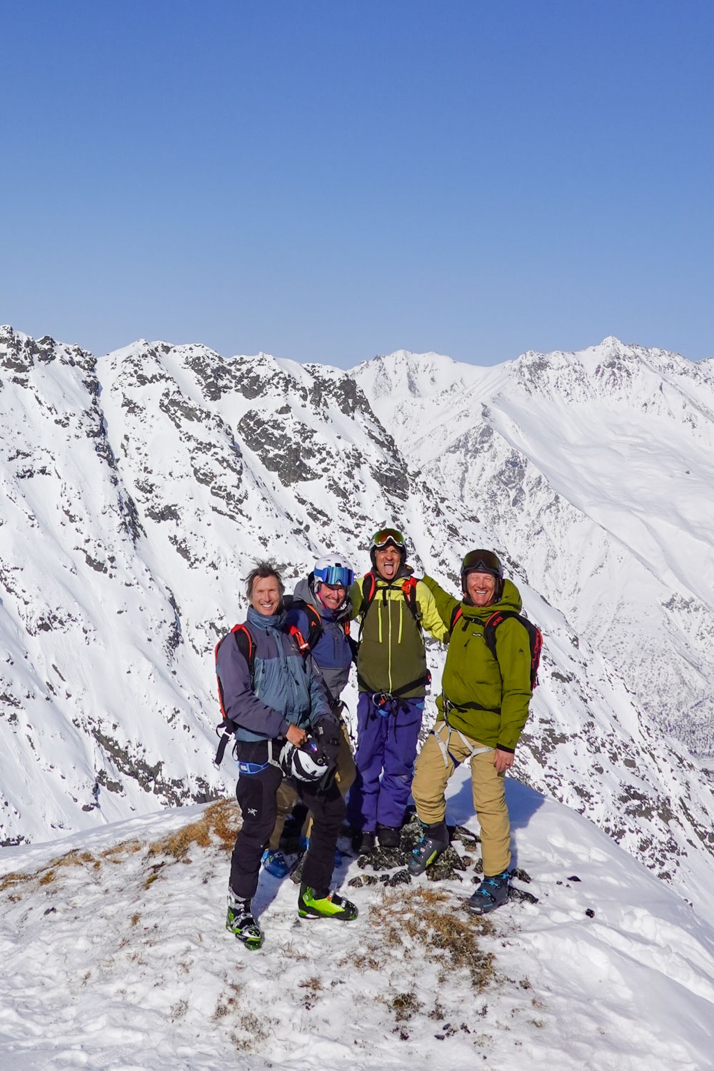 Four friends in ski gear pose on a snowy mountain summit